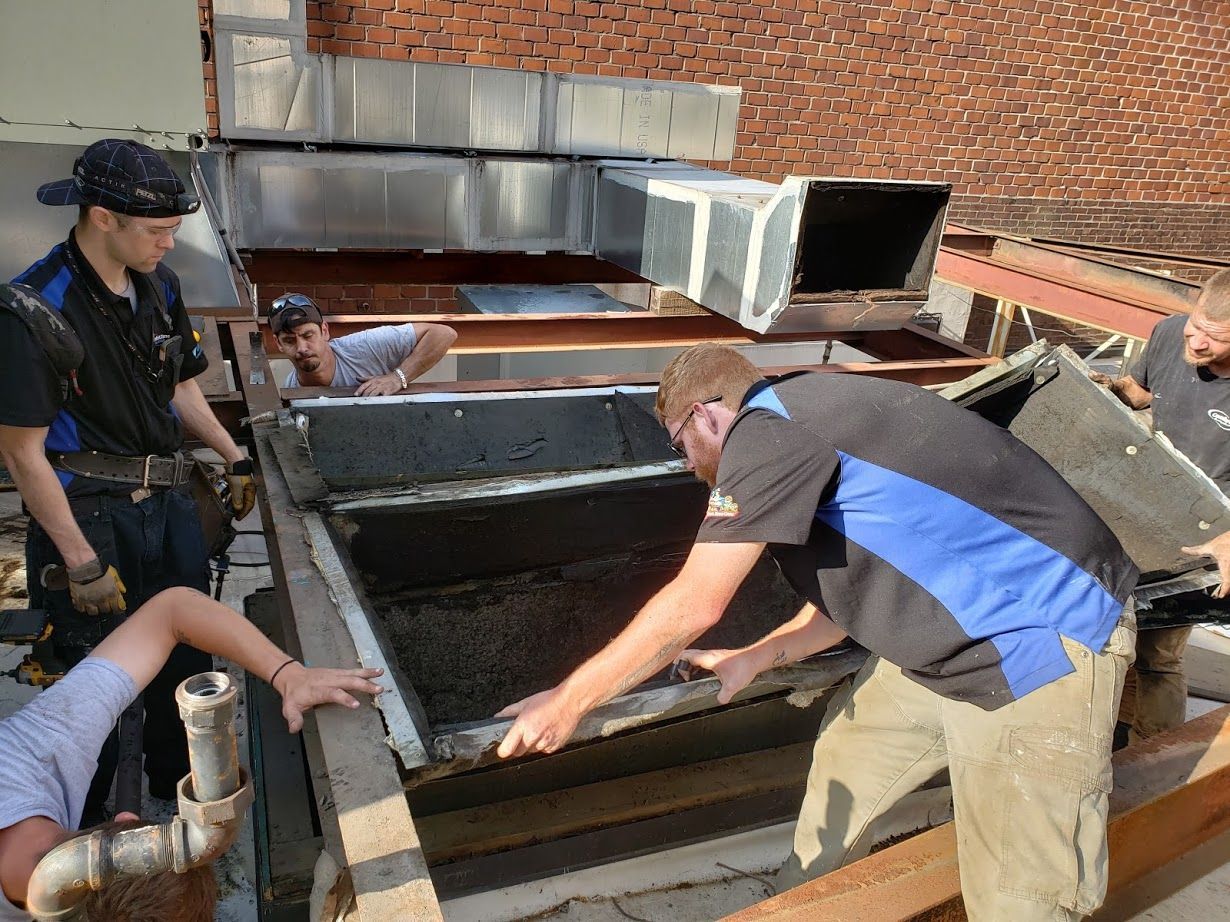 Construction workers removing a rooftop vent. They are wearing work clothes, working together on a sunny day.