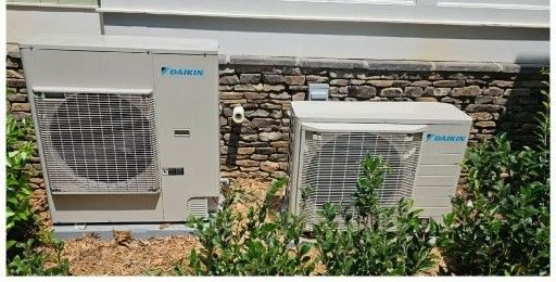 Technician standing beside an outdoor air conditioning unit, holding a tool.