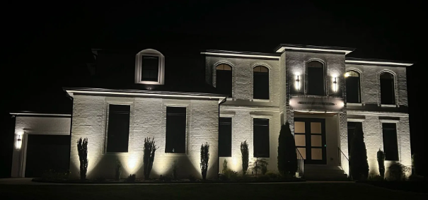 Night view of a large, lit-up stone house with several windows and a garage, set against a dark sky.