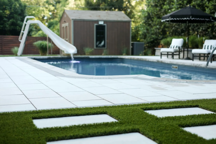 Backyard with pool, slide, shed, patio furniture, and square patches of artificial grass.