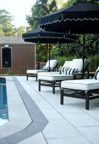 Poolside lounge area with black umbrellas, striped cushions, and wooden chaise lounges.