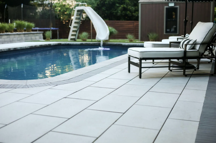 Swimming pool with a white slide, lounge chairs, and light gray stone patio.