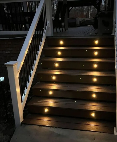 Wooden outdoor stairs illuminated by inset lights at night. White railing with black balusters.