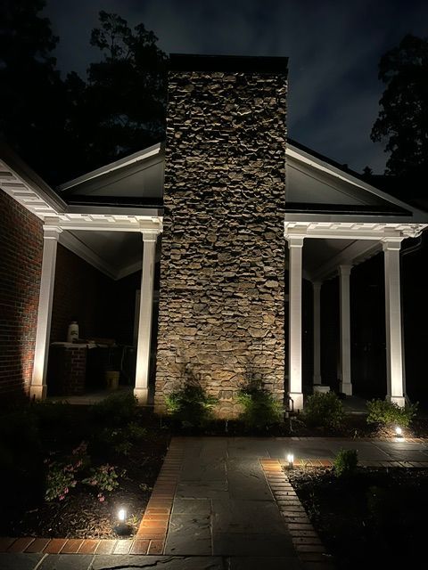 Lit stone chimney and walkway at night. Columns and low pathway lights illuminate the entrance.