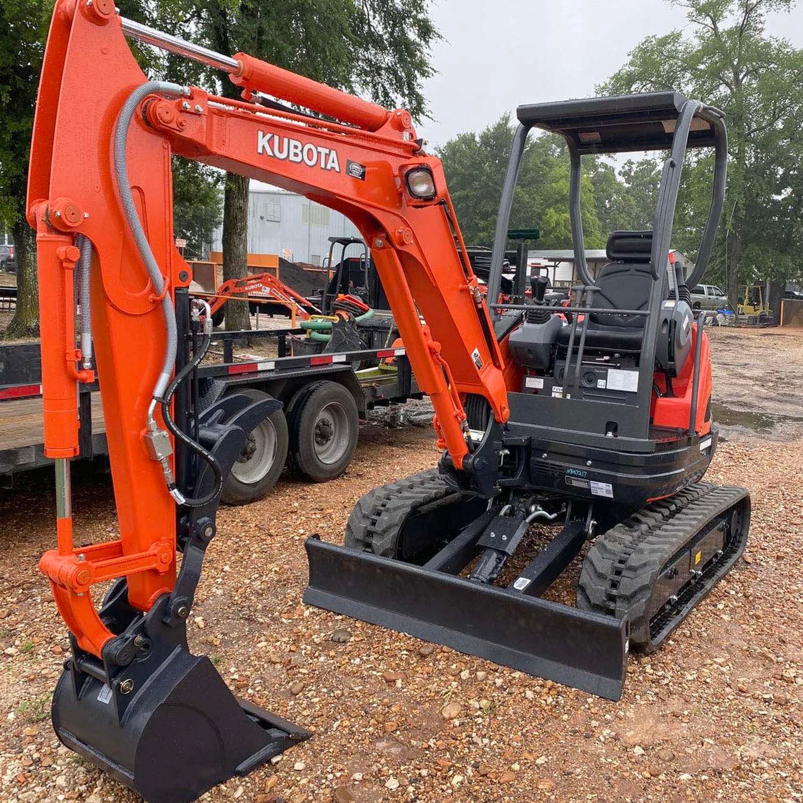 A small orange excavator is parked in a gravel lot