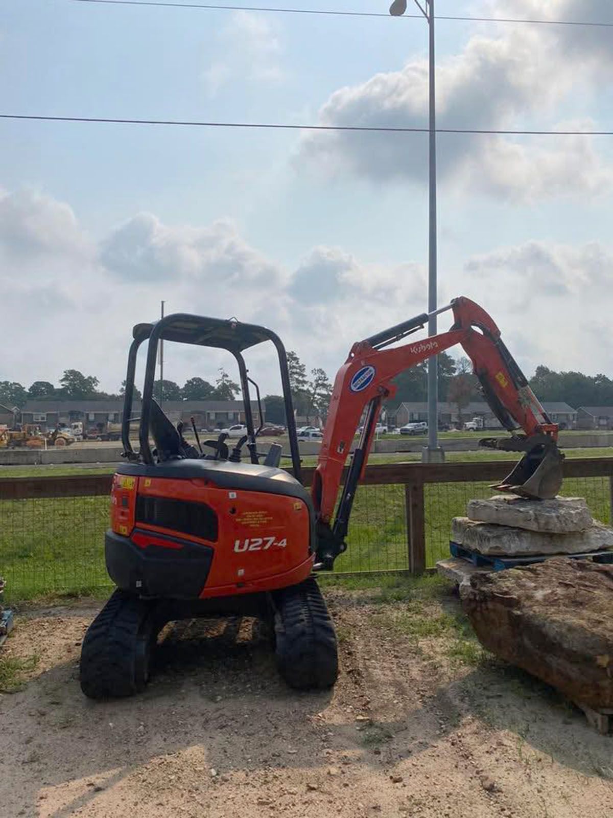 A small orange excavator is parked in a dirt lot