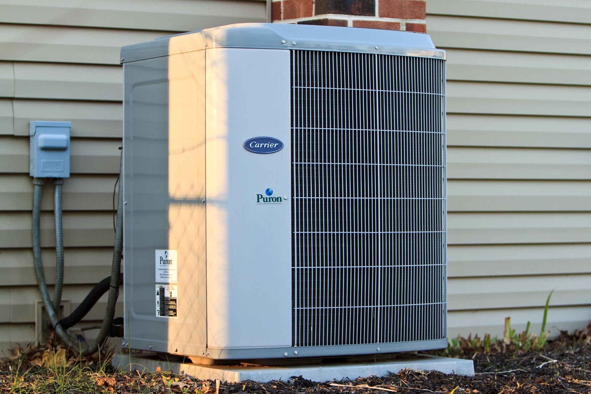 Carrier air conditioning unit against a beige wall. Blue logo and dark vertical grill.