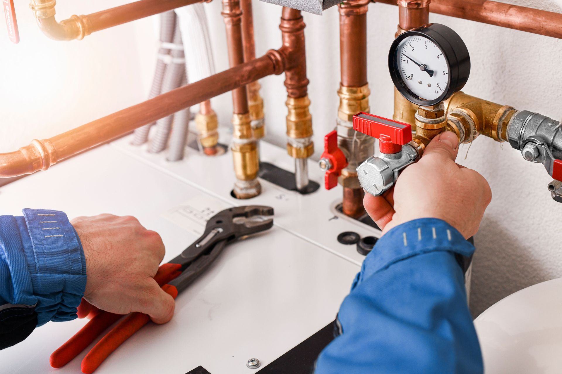 A plumber in blue shirt adjusts a valve on copper pipes with a wrench in a utility room.