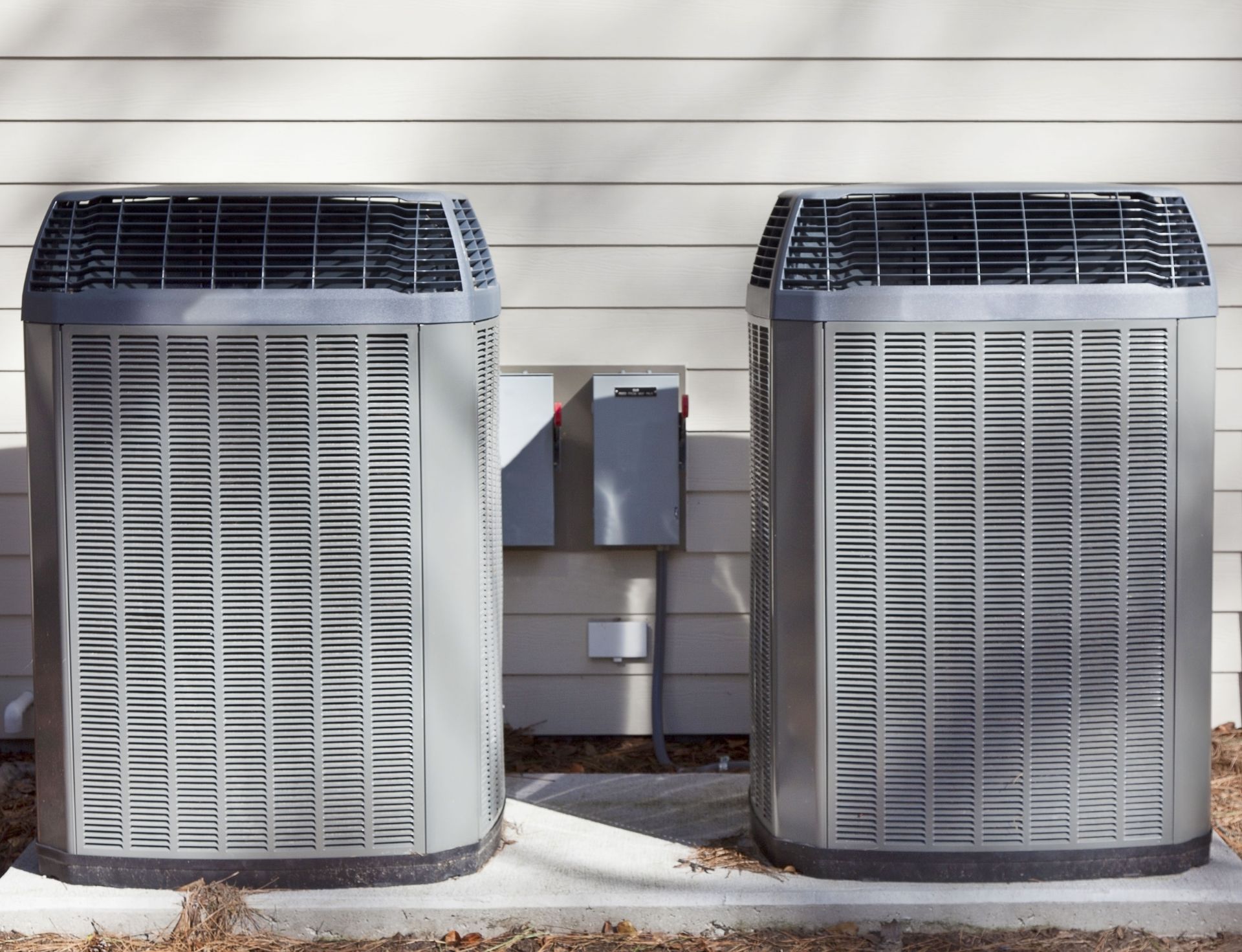 Two gray air conditioning units against a white wall.
