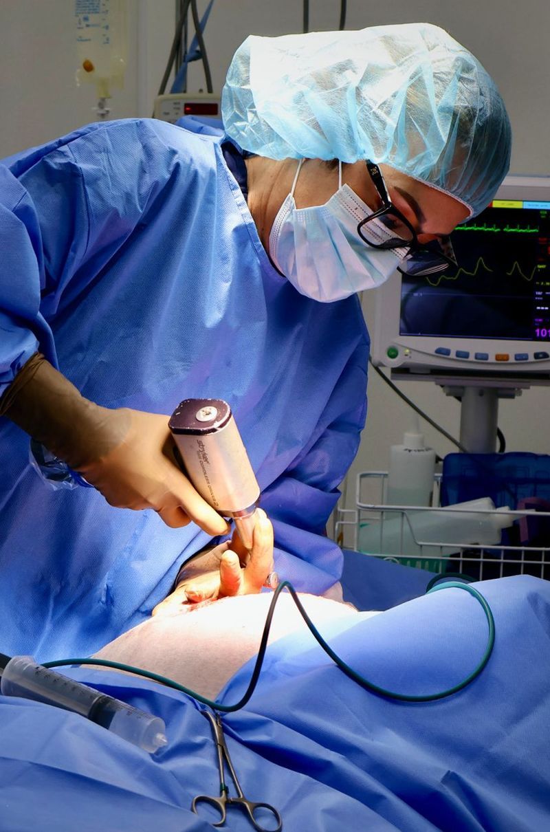 Surgeon in blue scrubs, mask, and cap using a medical device
