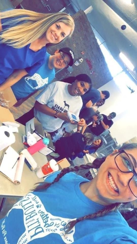Group of volunteers smiling, packing supplies at a table; various skin tones; blue shirts, casual setting.