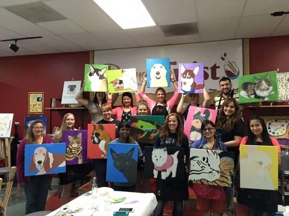 Group of people at a painting event, each holding up a canvas with dog paintings.