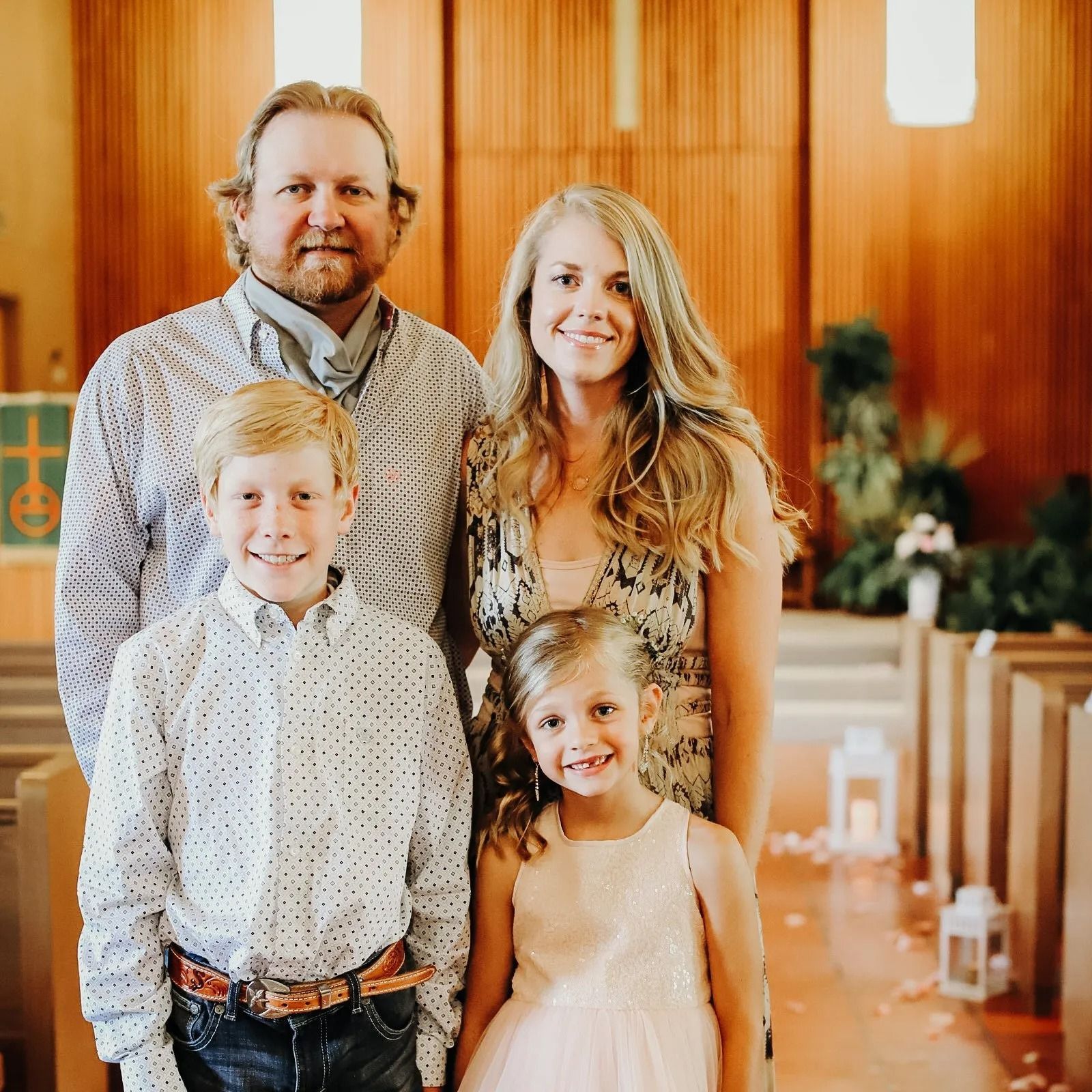 Family of four smiling in a church with wooden walls and pews.
