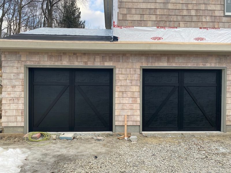 Two black garage doors with diagonal cross design in a building with cedar shake siding.