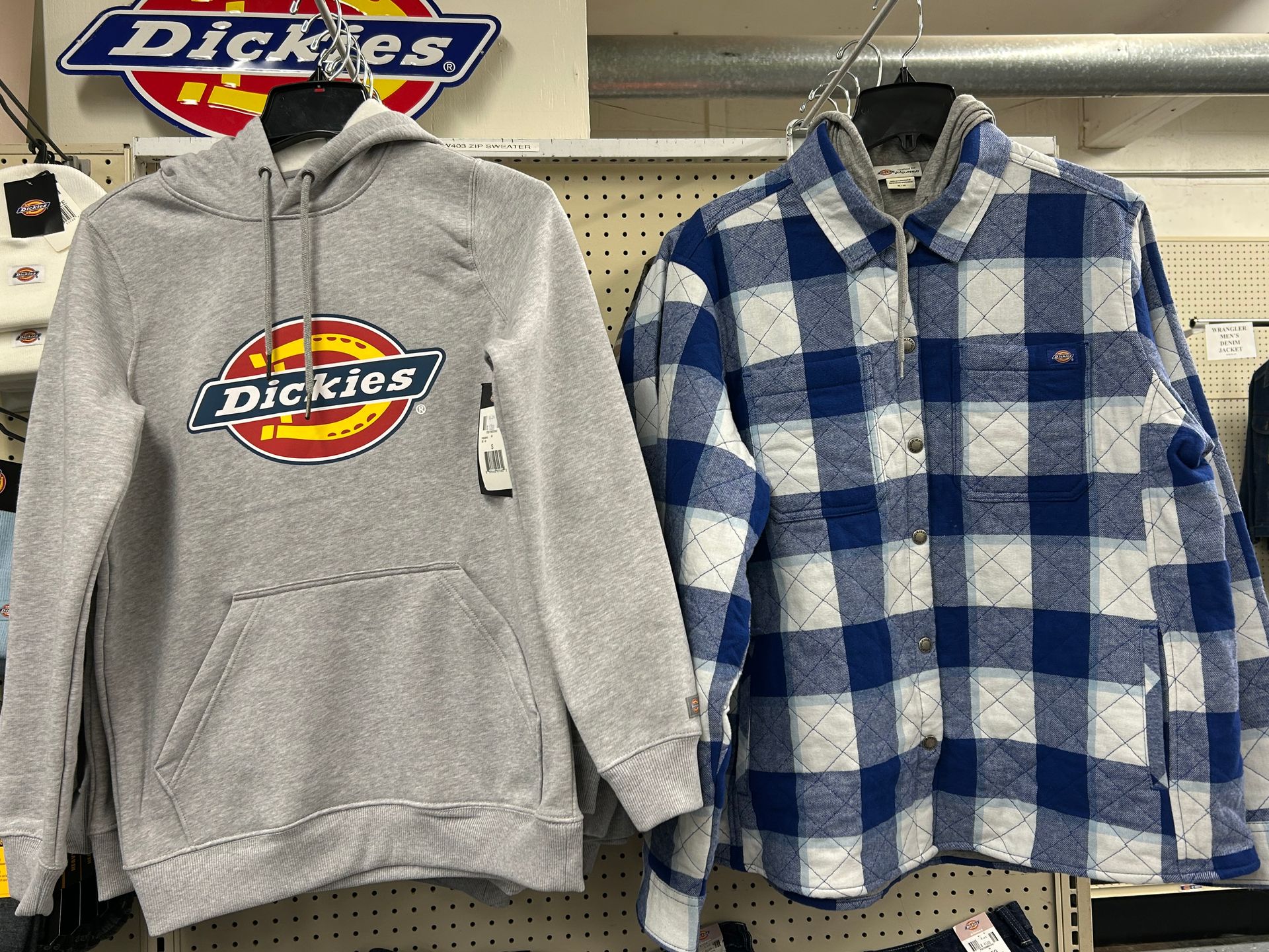 A hoodie and a plaid shirt are hanging on a rack in a store.