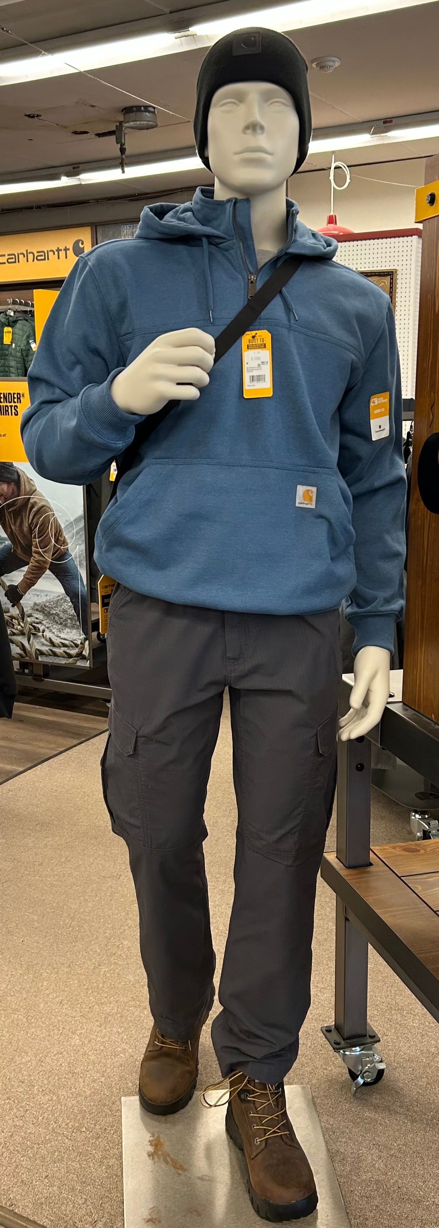 A mannequin wearing a blue hoodie and gray pants is standing in a store.