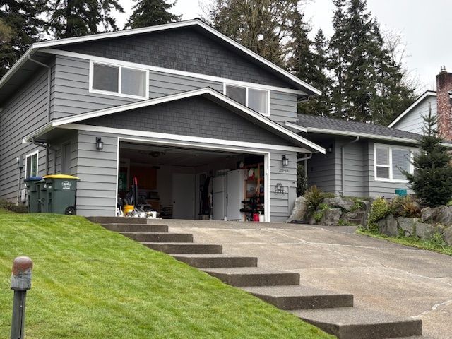 Gray house with open garage and stepped concrete driveway on a sloped lawn