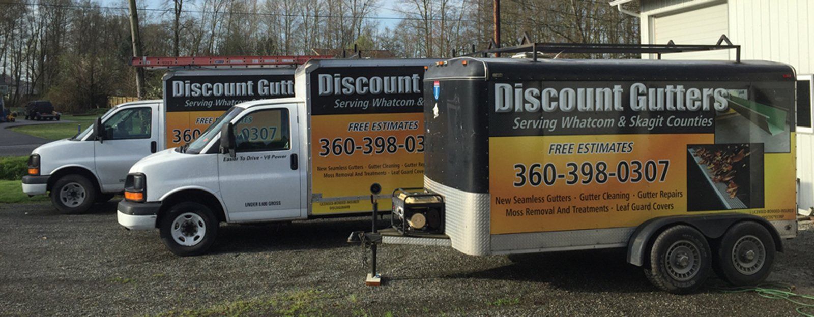 Two white Discount Gutter service vans parked outdoors beside a road sign.