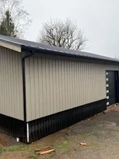 Beige metal building with dark trim and a black door, shown from the side on a cloudy day.