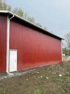 Red barn with white door on a muddy hillside under an overcast sky.
