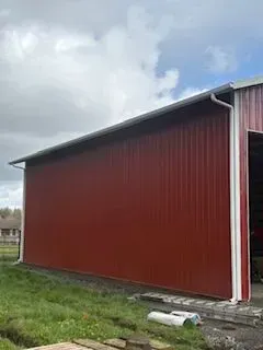 Red barn wall with white trim on a grassy farm under a cloudy sky