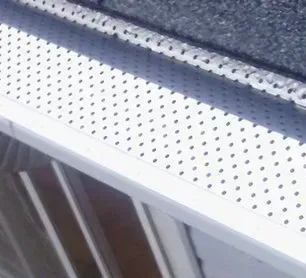 Close-up of a white perforated metal gutter or vent under a dark roof edge