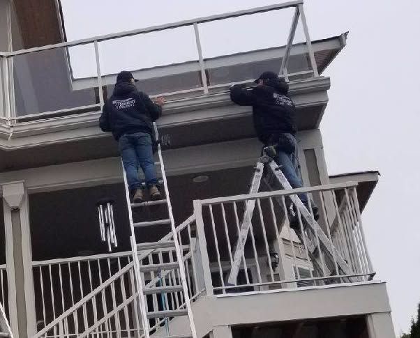 Two workers on ladders repairing a building balcony railing