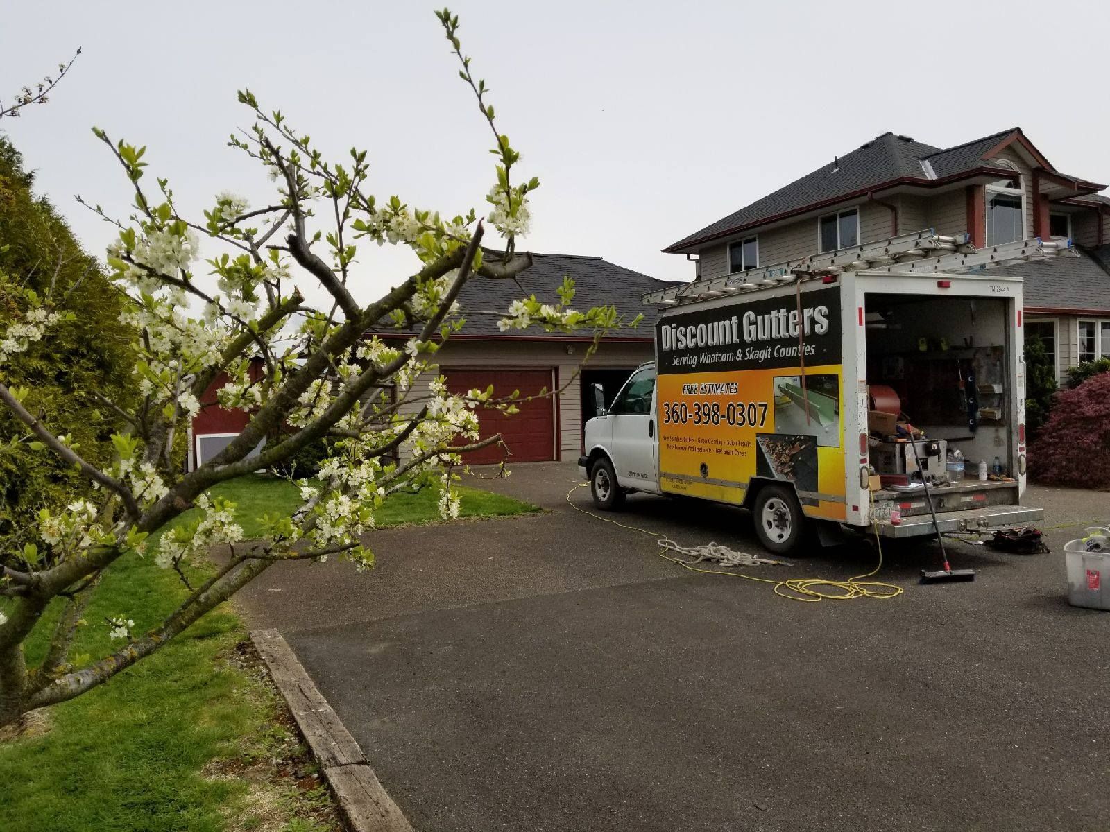 Yellow utility truck parked beside a house, with a fallen tree branch across the driveway.