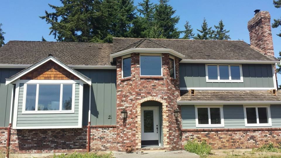 Two-story brick and siding house with white-trimmed windows, arched front door, and stone chimney.