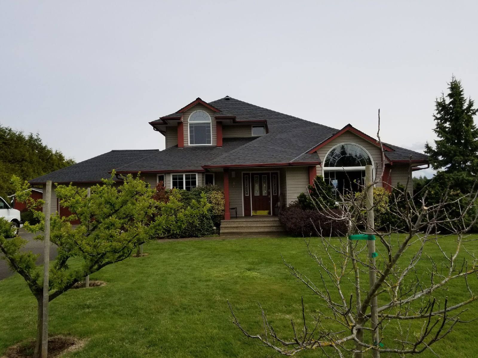Suburban house with a dark roof, red trim, and a large green lawn in front