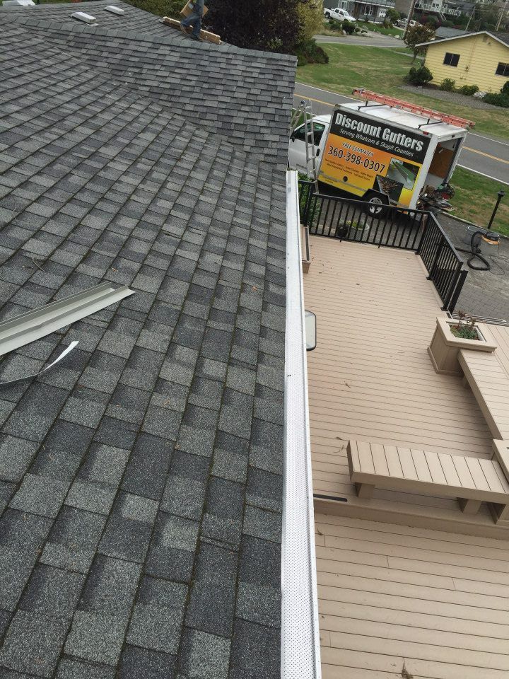 Roof and deck view with gray shingles, tan siding, and a sign on the adjacent building.