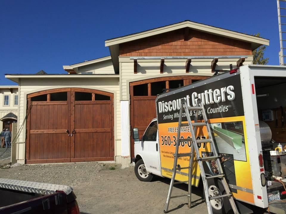 Truck with a ladder parked outside a house with a wooden garage door under a blue sky