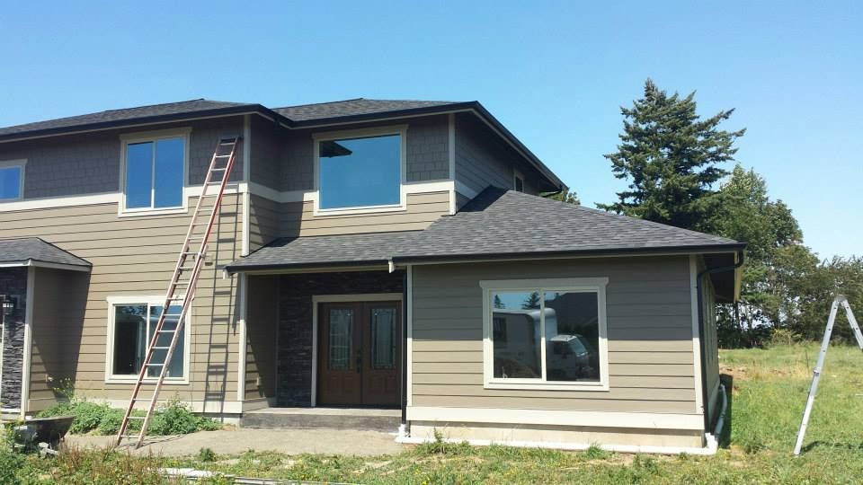 Two-story house with tan siding and a ladder leaning against the roof under a clear blue sky.