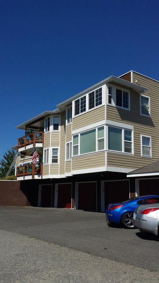 Three-story beige apartment building with white trim and parked cars in front on a sunny day