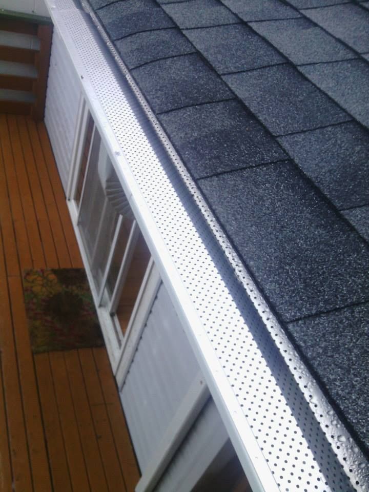 Gutter and white siding beside a sloped shingled roof, viewed from above a wooden deck.