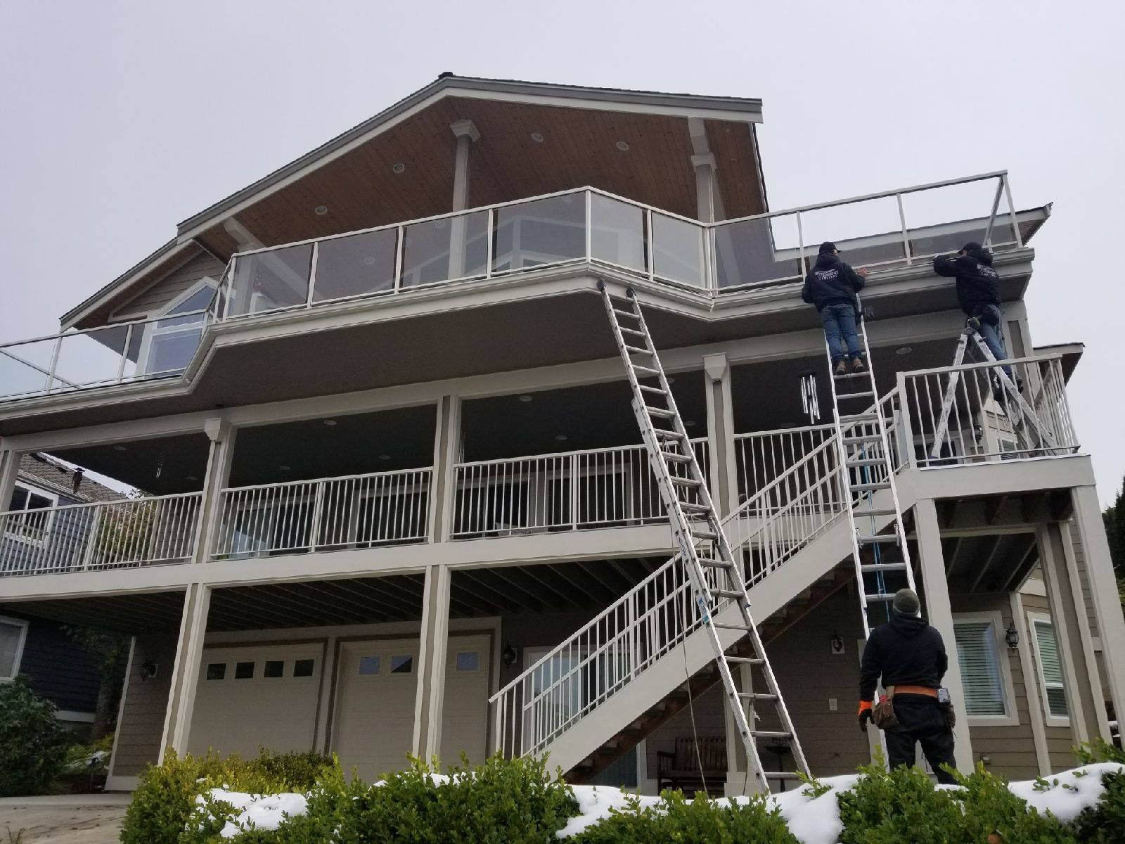 Workers on ladders repairing a two-story house roof and exterior siding