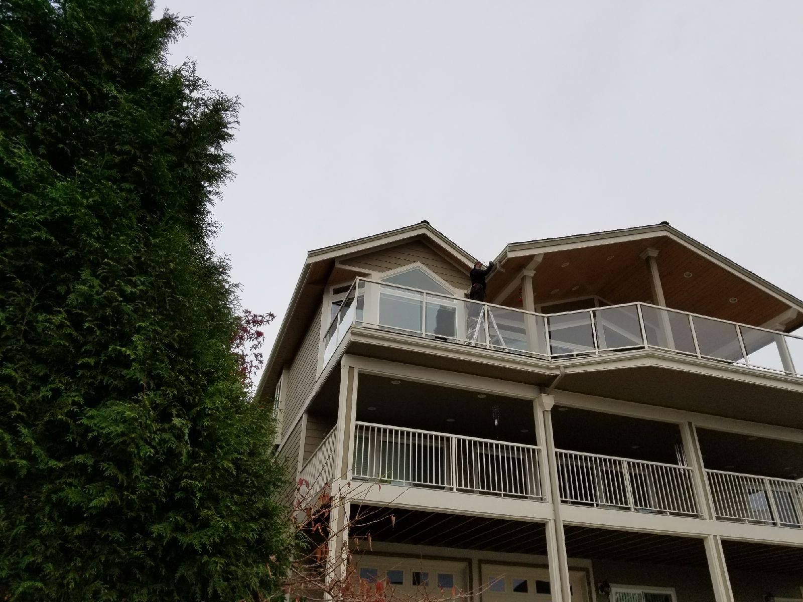 Multi-story house with balconies beside a tall tree under an overcast sky