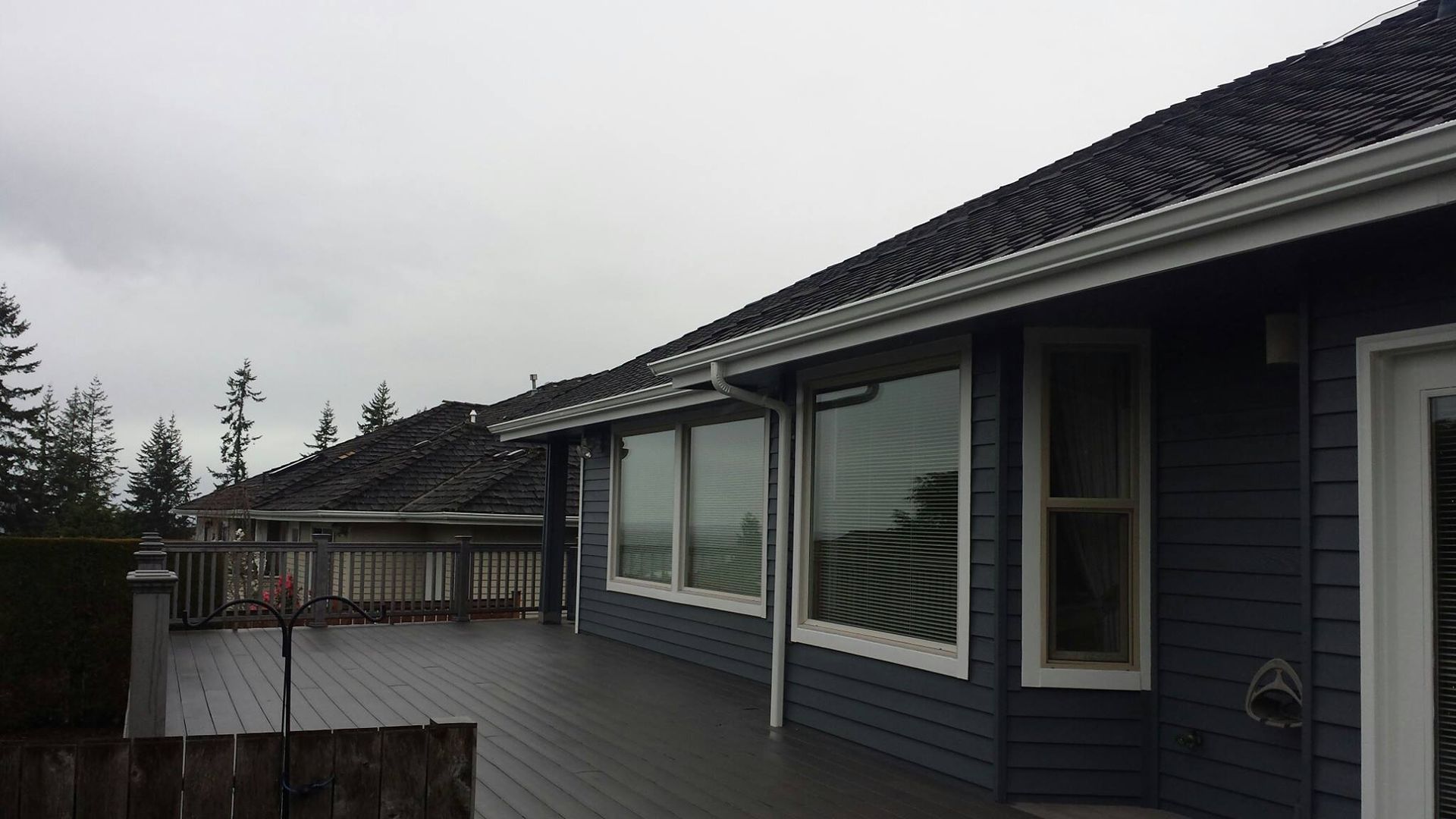 Modern house deck with large windows, gray siding, and a tiled roof on an overcast day