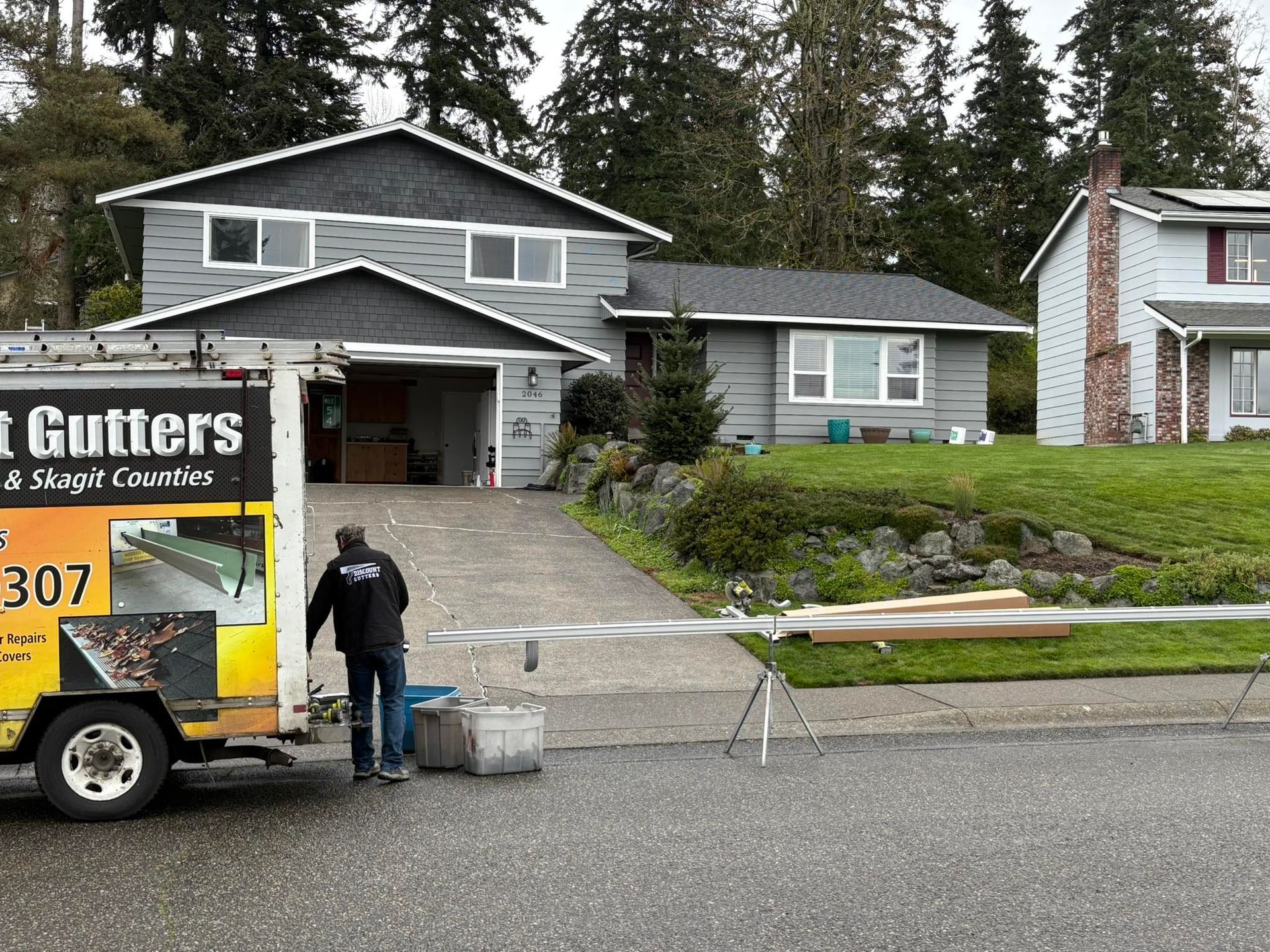 Worker loading equipment from a truck outside a suburban house with new gutters installed