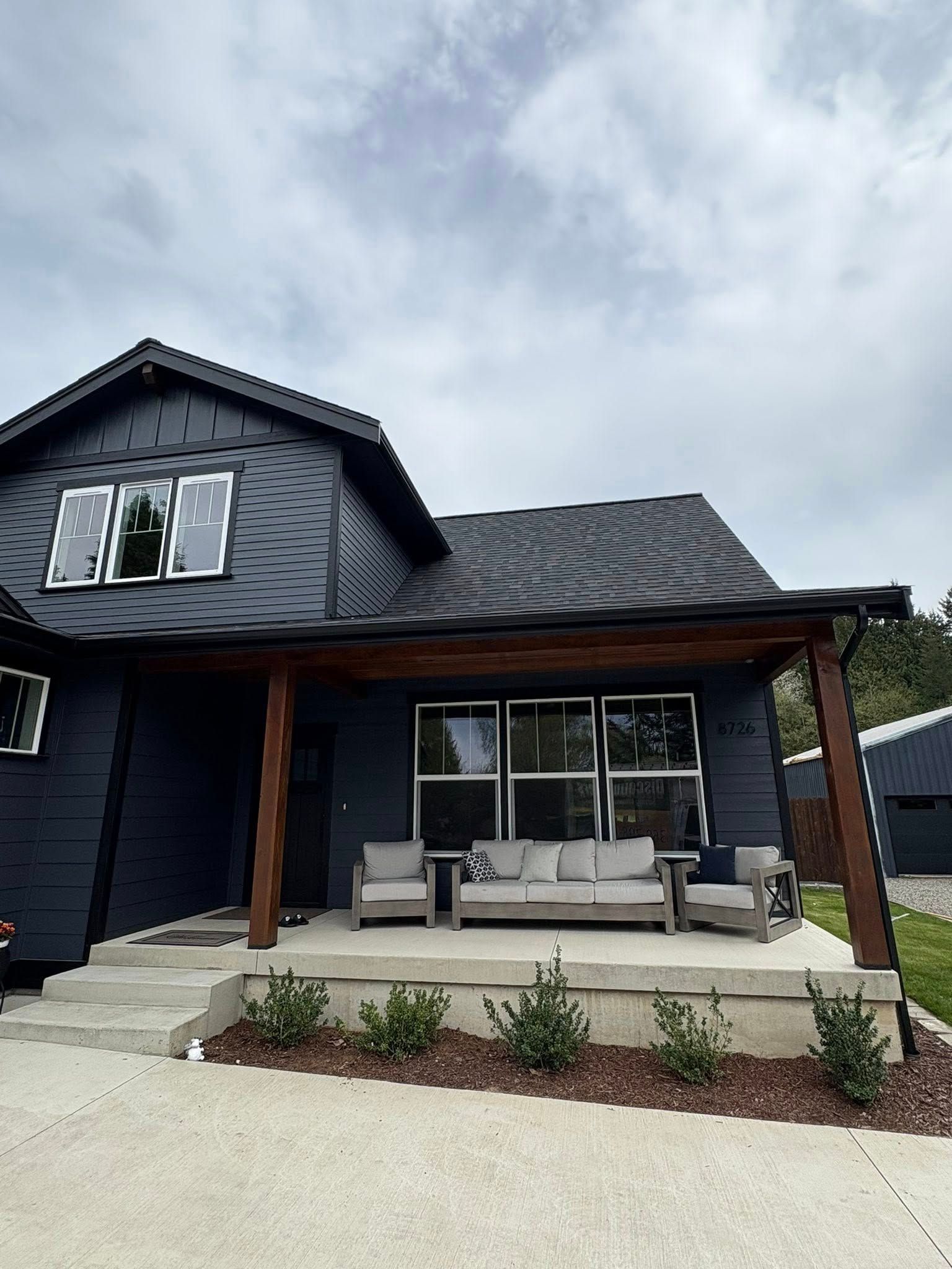 Modern dark-blue house with a covered front porch, outdoor seating, and a gravel driveway