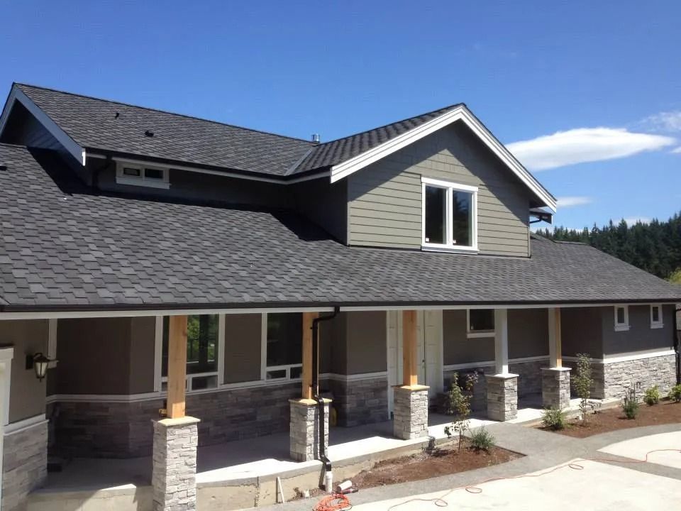Modern house exterior with gray roof, beige siding, and a covered front porch with stone columns