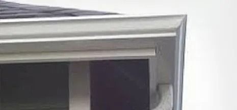 Close-up of a white window frame and gray roof edge against a light wall.