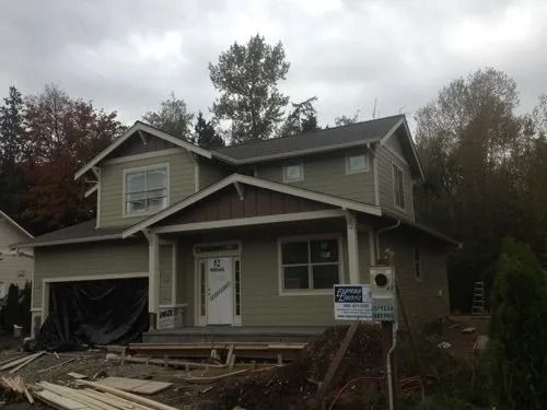 Partially built house with exposed framing, debris in front, and a work sign by the entrance