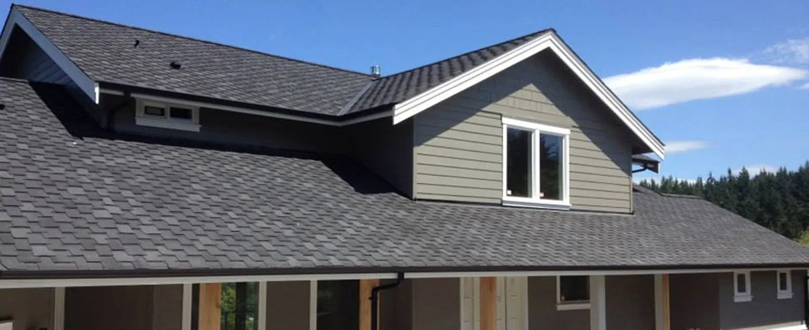 Suburban house exterior with gray siding, dark shingle roof, and white-trimmed windows under a blue sky