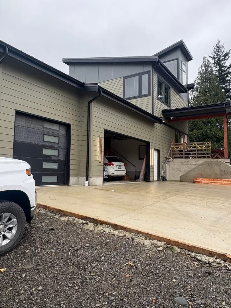 Modern house exterior with open garage, driveway, and parked vehicle partly visible under overcast skies