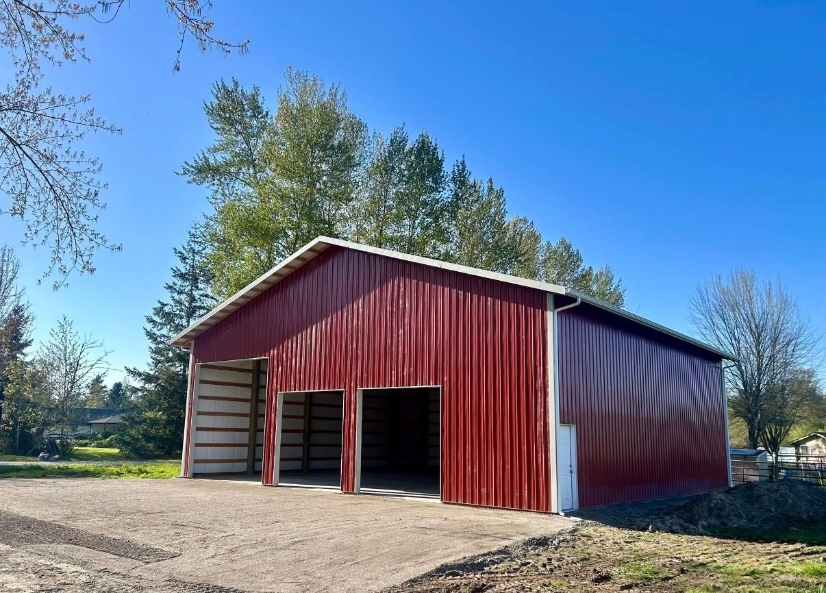 Red barn with open doors on a gravel lot under a clear blue sky, surrounded by trees
