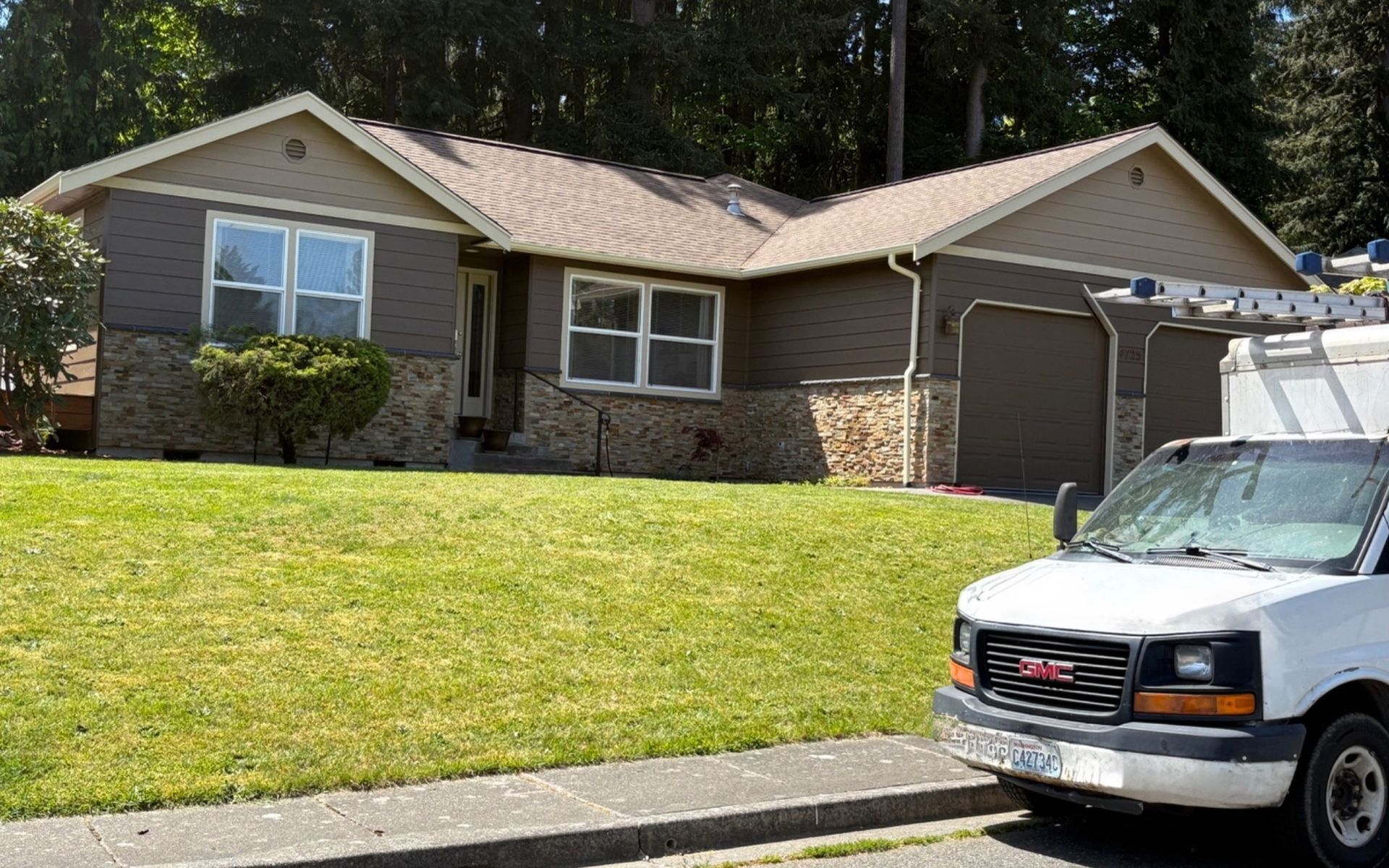 Single-story suburban house with tan brick, green lawn, and a white service van parked in the driveway.