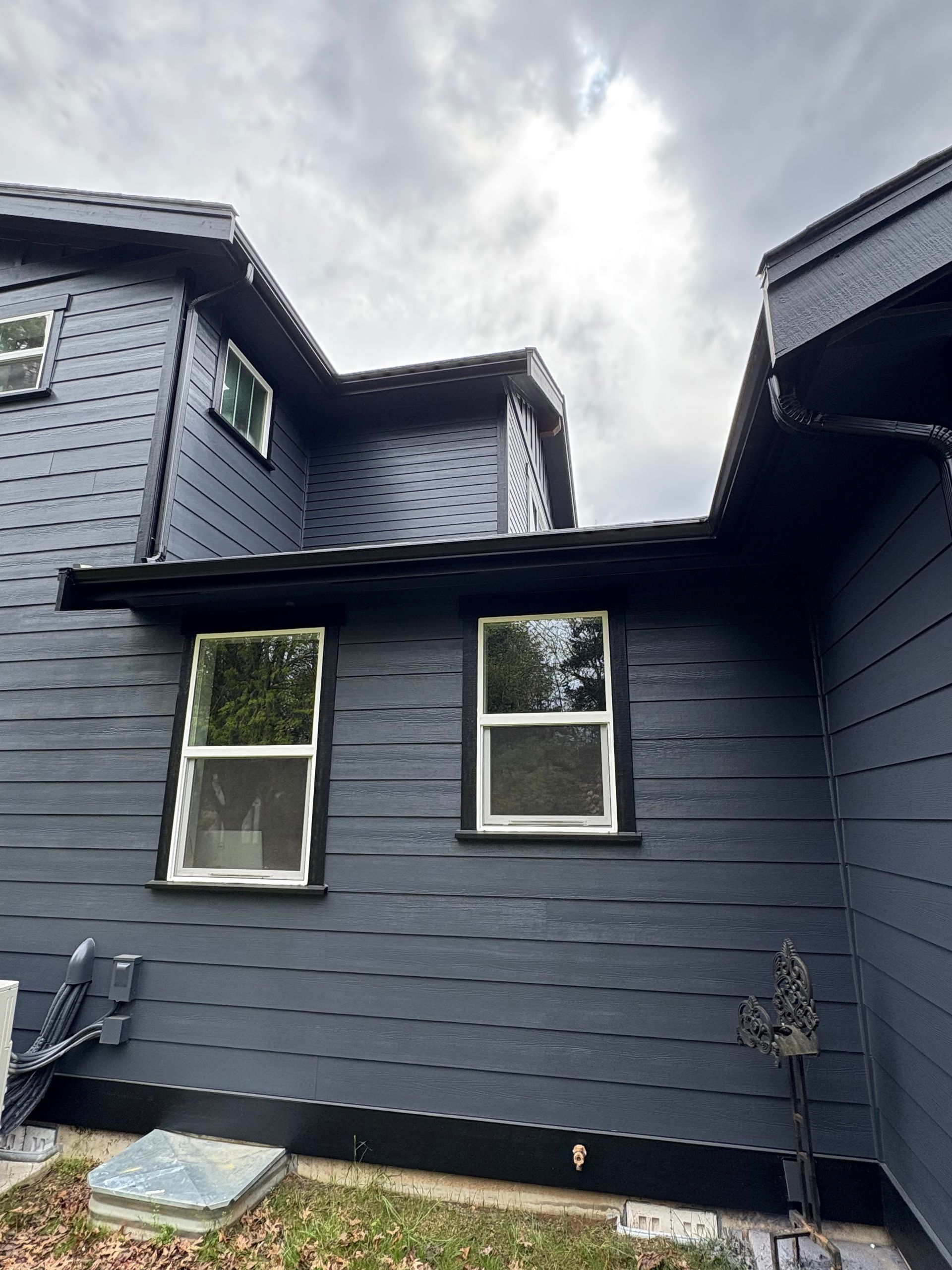 Dark blue house exterior with two windows and a small overhang under cloudy sky