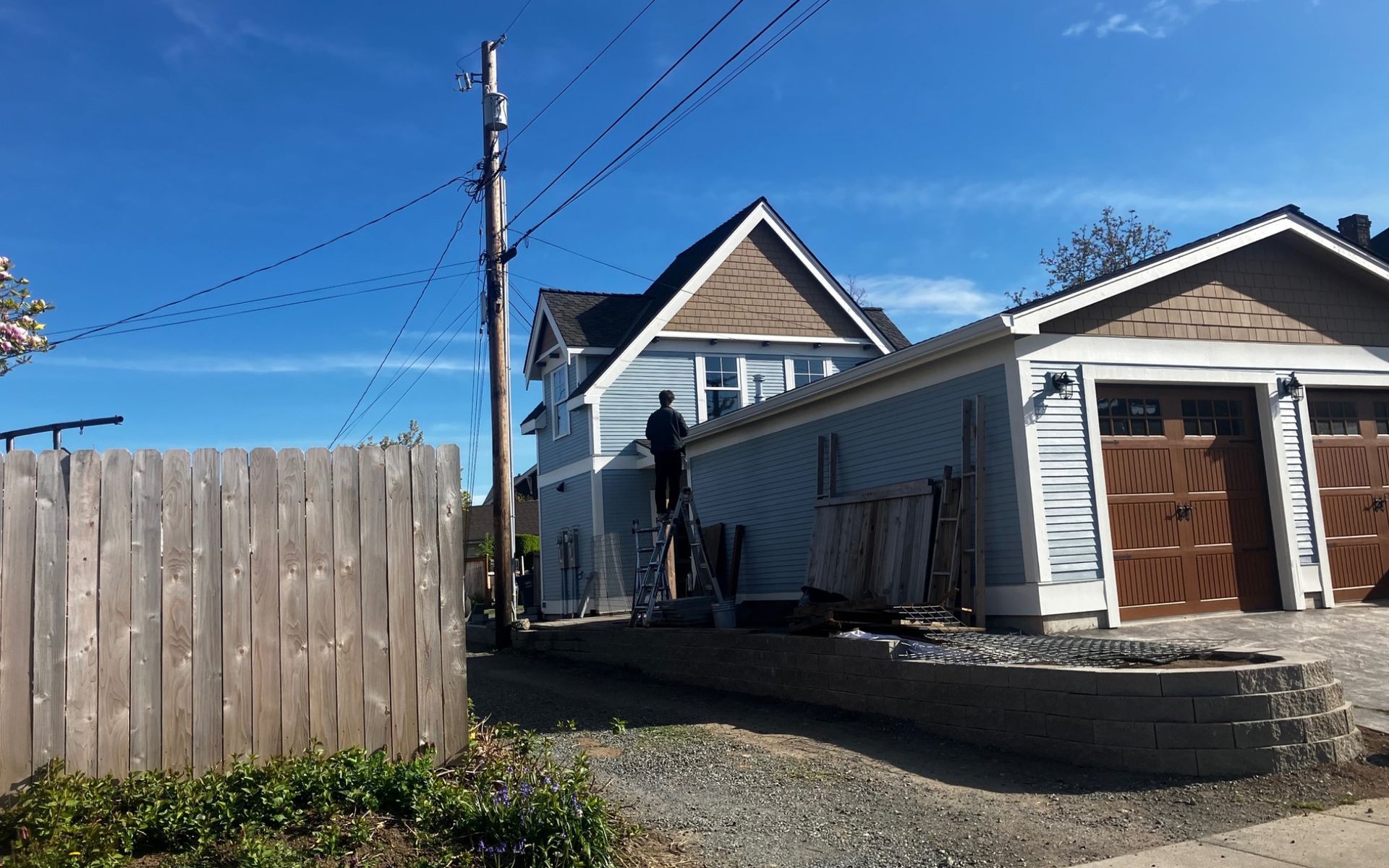 Residential backyard with house, wooden fence, garage, and clear blue sky