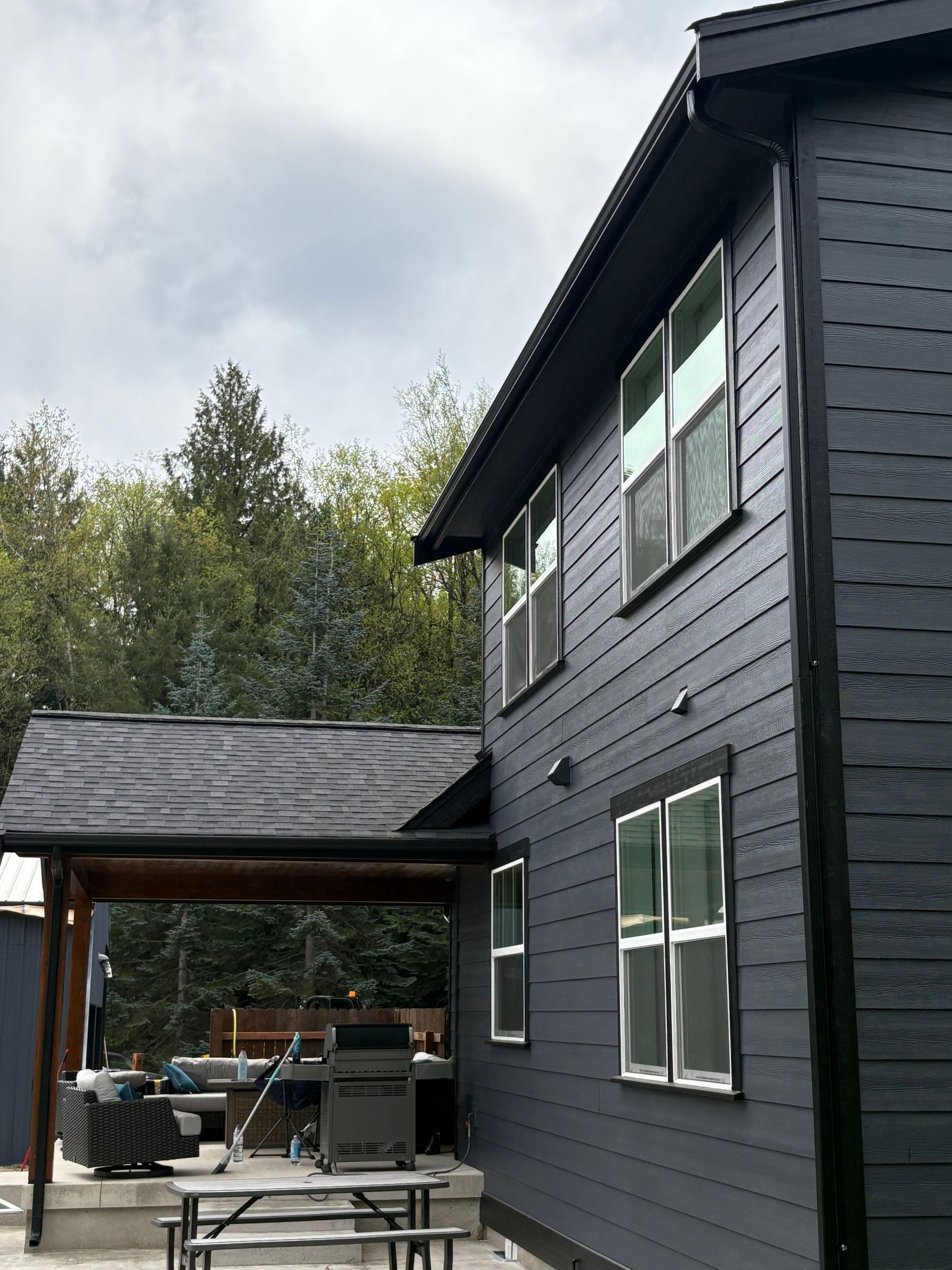 Dark gray house exterior with screened patio and outdoor seating under a cloudy sky